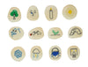 A set of twelve smooth, polished river stones arranged in a 3x4 grid on a white background. Each stone is hand-painted with a simple illustration representing a season or concept: a green tree, a sad face with a tear, a burning candle, a yellow sun, a shark, hands washing, a green sprout, a stone arch, a blue snowflake, rain with lightning, a blue bucket, and a stone castle.