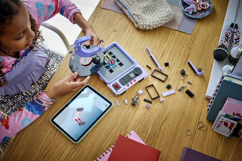 A young builder assembling the LEGO Olivia Rodrigo's Concert Moon set at a desk using the LEGO Builder app on a tablet
