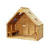 A small wooden A-frame playhouse or cabin with built-in benches, shown outdoors in a wooded forest setting with trees and fallen leaves around it.