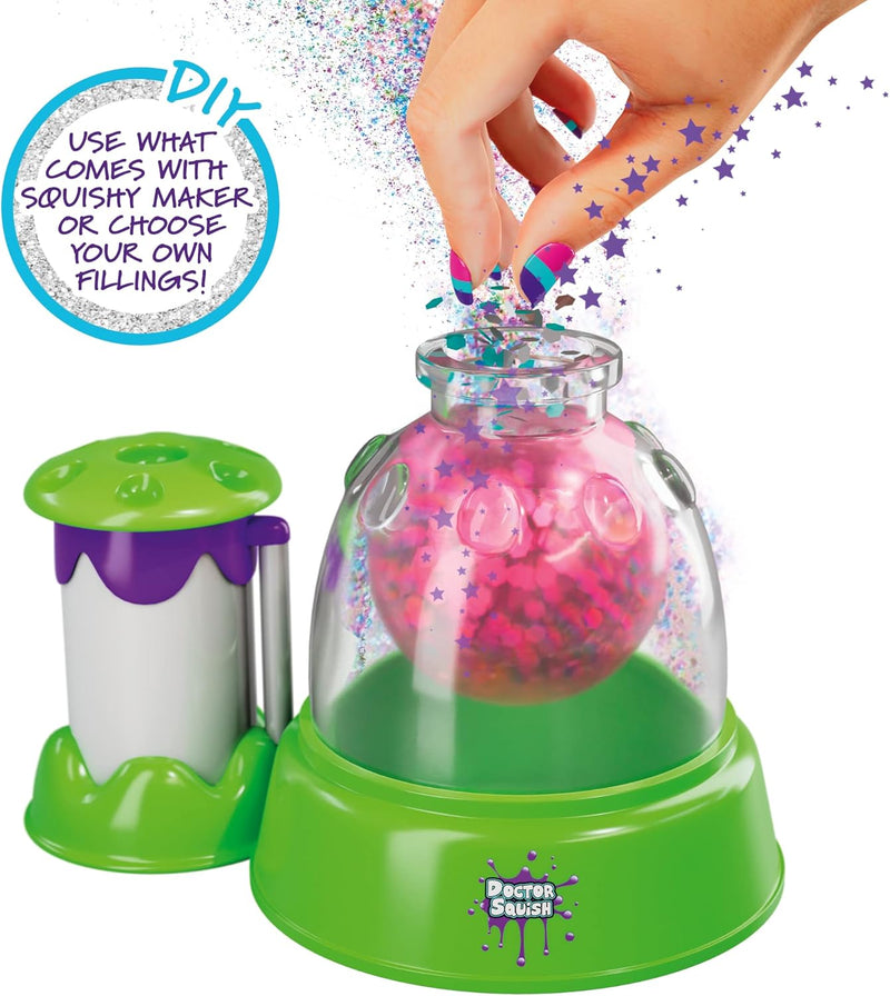 Doctor Seuss DIY Squishy Maker toy set with a green and purple base, a clear dome, and a pink glittery ball inside, shown with a hand inserting a small piece and a separate green-and-purple accessory container on a white background.