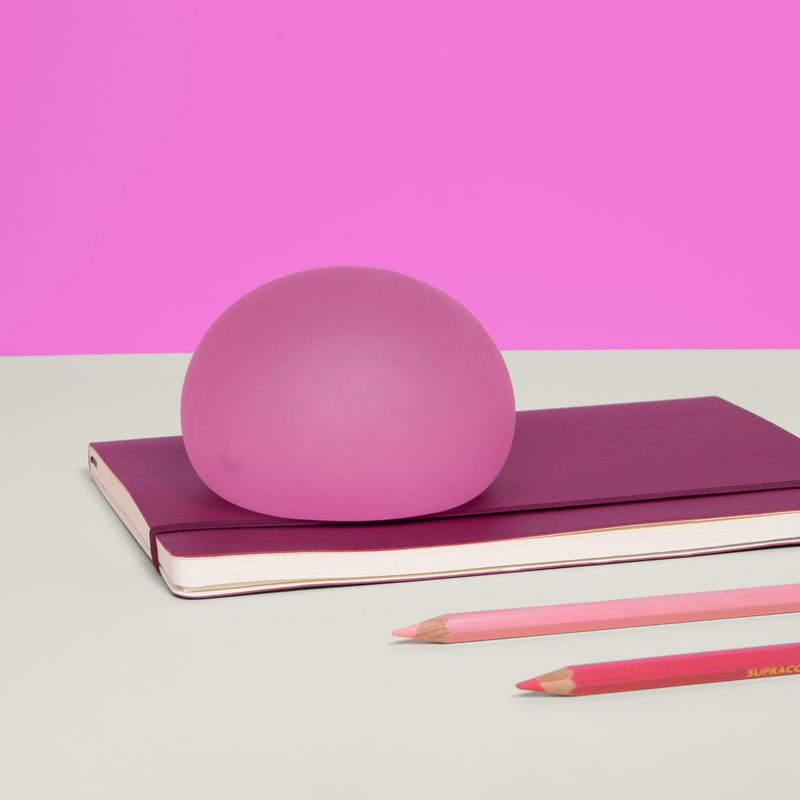 Speks Gump Jumbo Moon Jelly stress ball resting on a maroon notebook with pencils
