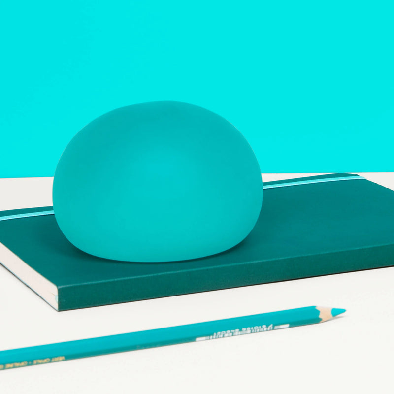 Speks Gump Jumbo Sea Glass stress ball resting on a teal notebook with pencils
