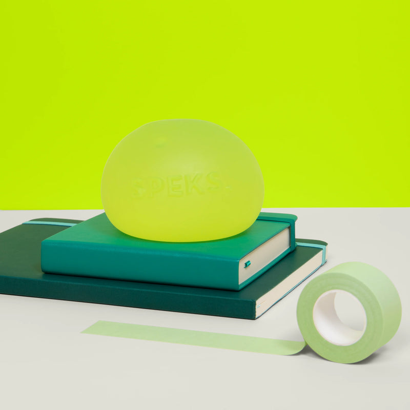 Speks Gump Jumbo Algae stress ball resting on stacked teal notebooks
