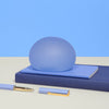 Speks Gump Jumbo Dew stress ball resting on stacked blue notebooks with pens
