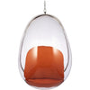 A modern egg-shaped hanging pod chair with a clear transparent shell, a metallic silver frame, and an orange seat cushion, suspended by a chain against a white background.