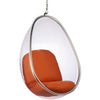 Clear hanging egg chair with orange cushioned seat and backrest, suspended by a metal chain with a chrome frame, on a white background.