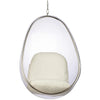 A modern egg-shaped hanging chair with a clear transparent plastic shell, a silver metal frame, and a thick cream-colored cushion inside, suspended by a chain against a plain white background.