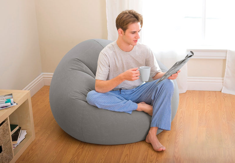 man sat on grey bean bag in pjamas drinking a hot drink and reading a magazine