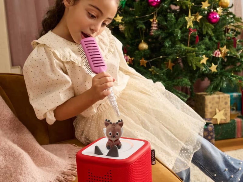 Child beside a Christmas tree with The Little Reindeer’s Christmas Wish Tonie on a red Toniebox